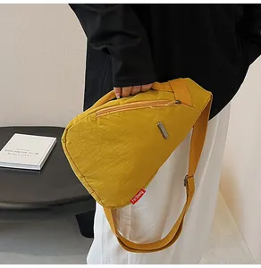 Detail of yellow canvas crossbody bag featuring a metal logo plate and zip pocket
