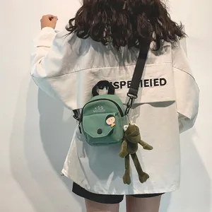 Detail of light green canvas mini crossbody bag with cute plush frog pendant and adjustable strap