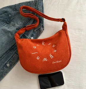 Detail of orange corduroy crescent bag with white fashion embroidery and adjustable strap