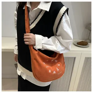 Primer plano del bolso bandolera de pana naranja con bordado detallado de letras
