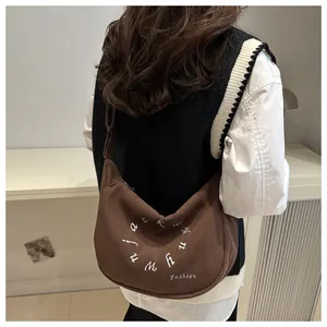 Detalle de bolso hobo de pana marrón con bordado de letras blancas circulares en el hombro