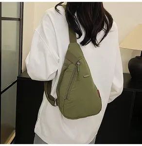 Rear view of an olive green canvas chest bag worn over a white hoodie by a model