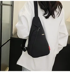 Detail view of a black nylon crossbody bag featuring a side zipper and red Reiseng woven label