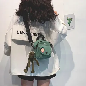 Green canvas mini crossbody bag featuring a cute cartoon face and brown frog plush pendant