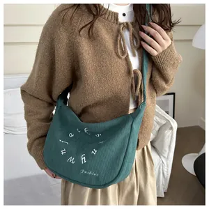 Primer plano de un bolso hobo de pana verde oscuro con letras bordadas en blanco