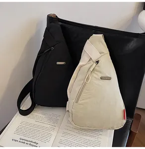Detail of minimalist nylon chest bags in black and beige on a leather chair with magazine