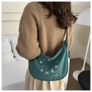 Detail view of dark green corduroy crescent bag with embroidery shown on shoulder