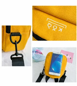 Detail of yellow canvas bag featuring logo print, black zipper, and adjustable strap