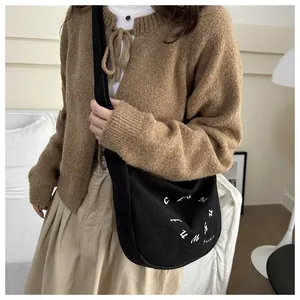 Detalle de bolso de pana negra con bordado blanco y cárdigan de punto marrón informal