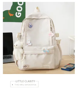 Dettaglio dello zaino in nylon crema con spille di cartoni animati e ciondolo a forma di orso