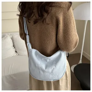 Detalle del bolso bandolera de pana azul claro con bordado blanco en superficie texturizada