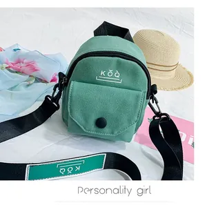 Detailed close-up of a mini green canvas crossbody bag with KǑQ logo on a white fabric surface