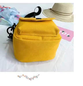 Detail of yellow canvas crossbody bag featuring a black snap button and shoulder strap