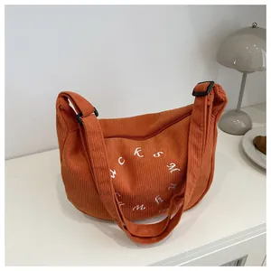 Detail of orange corduroy crescent bag featuring white embroidered letters and wide strap