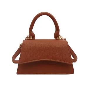 Minimalist brown pebbled leather trapezoid handbag with a bold curved top handle for women
