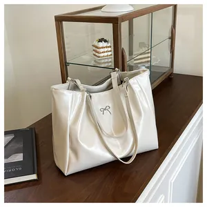 Détail du sac fourre-tout crème brillant avec nœud argenté et texture plissée chic