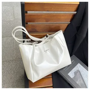 Détail d'un cabas en cuir verni blanc avec nœud argenté décoratif posé sur un banc en bois