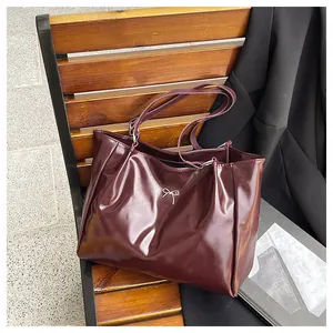 Détail d'un cabas en similicuir rouge avec boucle nœud argenté sur un banc en bois