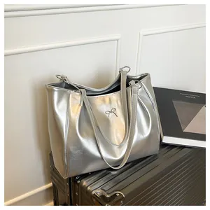 Détail d'un sac cabas argenté avec une boucle en métal en forme de nœud sur une valise