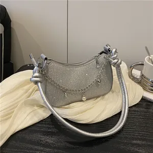 Sac bandoulière pailleté argenté avec poignée nouée et chaîne à breloques sur table