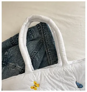 Gros plan sur les bretelles matelassées épaisses et la broderie papillon du sac blanc