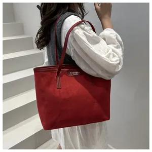 Detail view of a red suede tote bag featuring a leather brand tag and slender shoulder straps