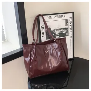 Détail d'un cabas bordeaux montrant la texture du cuir brillant et l'ornement en argent