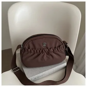 Brown nylon crescent crossbody bag featuring pleated design and wide canvas strap