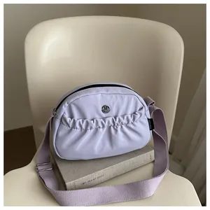 Light purple nylon crossbody bag with pleated front pocket and wide fabric shoulder strap