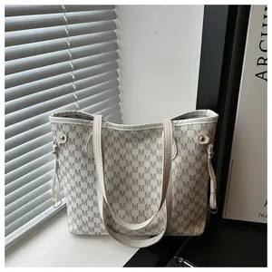 Detail of cream tote bag with black M-letter pattern and golden drawstring hardware