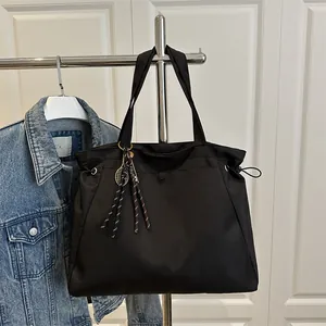 Large black tote bag with drawstring side and tennis racket pendant for daily commute
