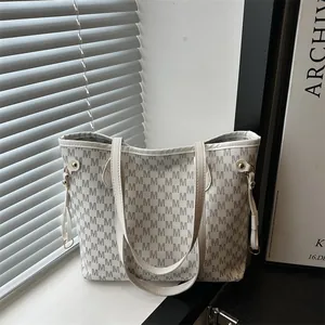 Minimalist beige tote bag with M-pattern monogram and gold buckles on a window sill