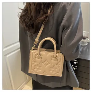 Detail of beige tote bag featuring floral embossing and adjustable shoulder strap worn by model