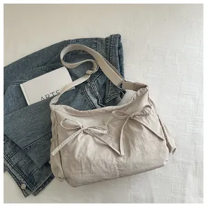 Detail of beige nylon pleated crossbody bag featuring decorative bows and side pocket