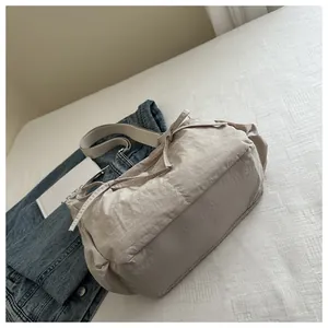 Detail of light beige pleated messenger bag with decorative side bow on white bedding