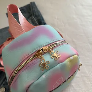 Close-up of a gradient tie-dye mini backpack featuring flower-shaped golden zipper pulls