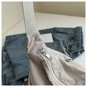 Detailed close-up of beige crescent bag featuring pleated nylon texture and silver zipper