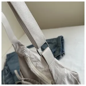 Close-up of beige pleated messenger bag showing silver metal ring and woven strap detail