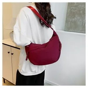 Model view showing the burgundy nylon crescent crossbody bag with woven knot zipper pull
