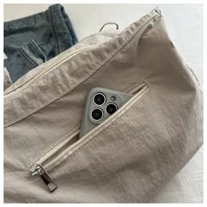 Detail of the front zipper pocket on a beige ruched nylon bag holding a smartphone