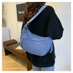 Model view of a light blue nylon crescent bag with woven zipper pull and wide strap