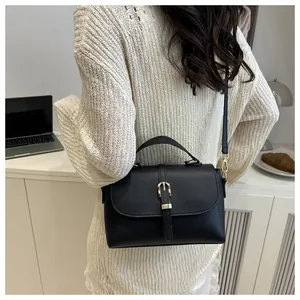 Close-up of a black lychee leather crossbody bag worn by a model in a cozy cafe setting