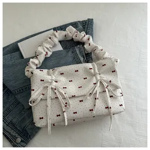 Detail of white pleated handbag with red bows and ruffles on a blue denim background