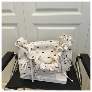 Detail view of white canvas shoulder bag with red bow prints and ruffled cloud handle