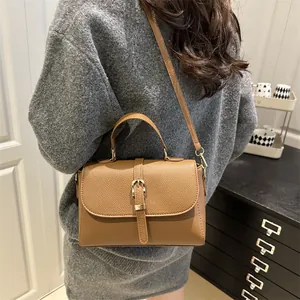 Brown lychee pattern crossbody bag with gold buckle shown on model in cozy room