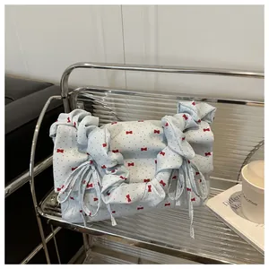 Close-up of light blue fabric shoulder bag with red bows and pleated strap on a shelf