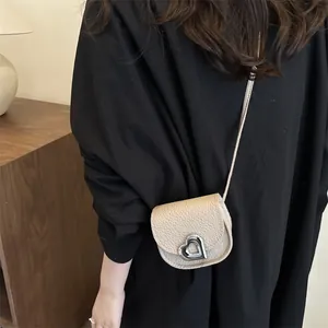 Detail of a mini beige saddle bag with lychee texture and silver heart buckle on a model
