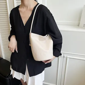 Sac seau chic en cuir beige grainé avec chaîne argentée présenté porté par un mannequin