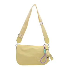 Pale yellow nylon crossbody bag with wide strap and embroidered logo on white background