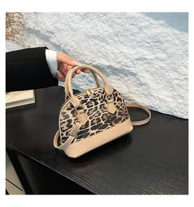 Close-up of leopard print dome bag with beige leather handles and gold-tone zippers